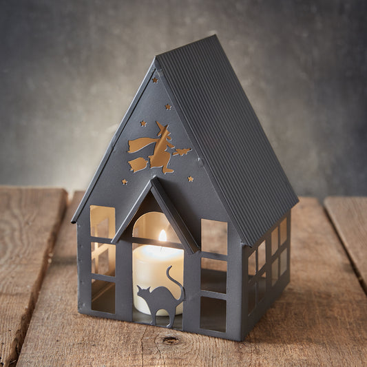 House-shaped lantern with cut-out designs of a cat and a witch on a wooden surface.