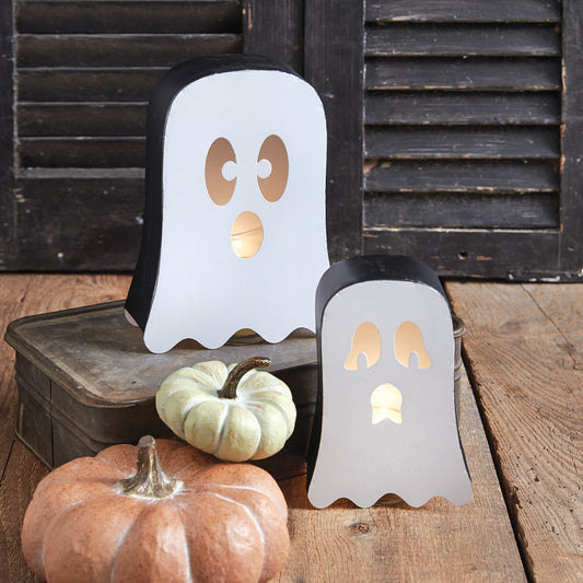 Two ghost-shaped candle holders with small pumpkins on a wooden surface.