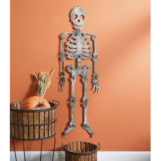 Metal skeleton wall decoration against an orange wall with a wooden basket and pumpkin.